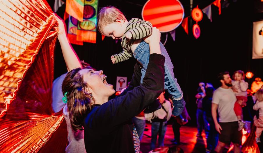 woman holds her baby in the air on dance floor at Baby Rave.