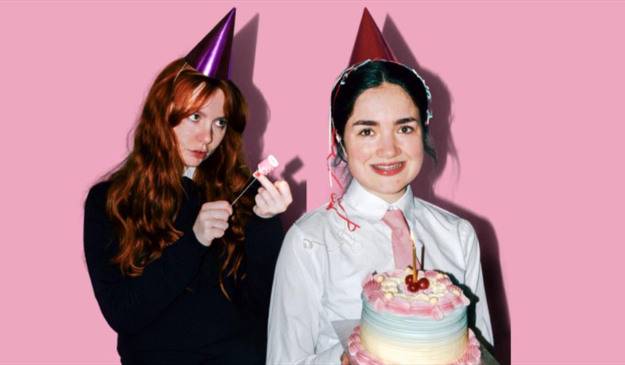 Two white women in party hats, one is holding a birthday cake.