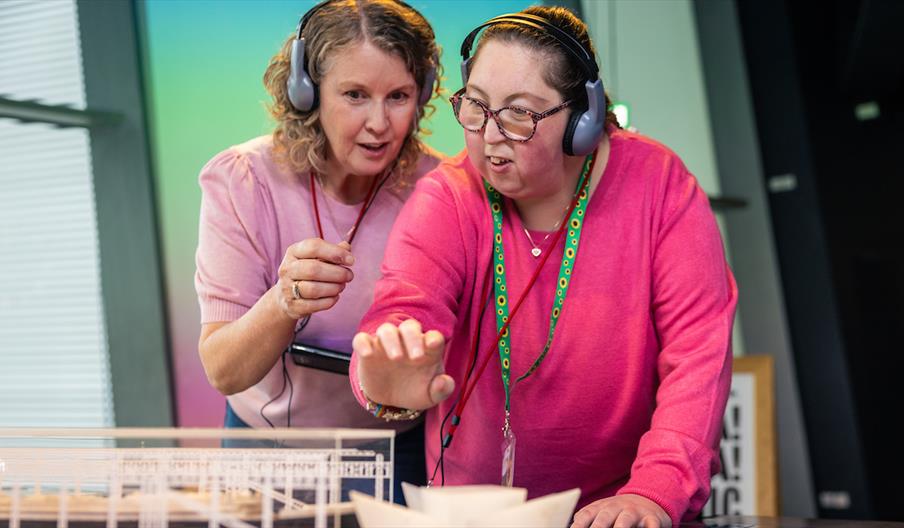 Two visitors wearing audio headsets interact with a touchscreen display while exploring the Titanic Experience at Titanic Belfast.