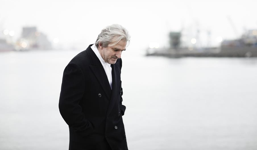 Barry Douglas walks with hes head cast downward in front of a grey foggy marina