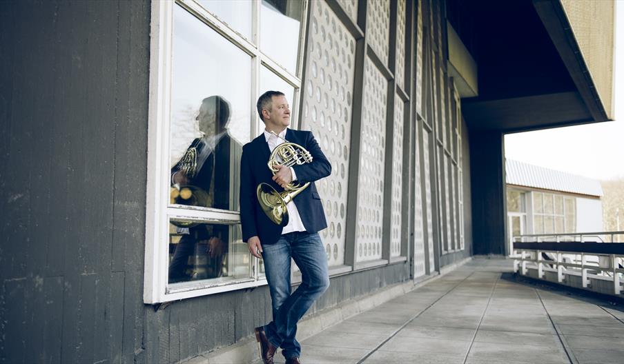 French horn player, Stefan Dohr, stands outside a concert hall holding his Horn
