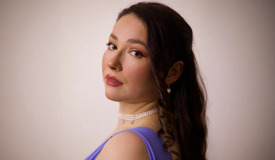 A woman in a purple dress looks over her shoulder toward the camera