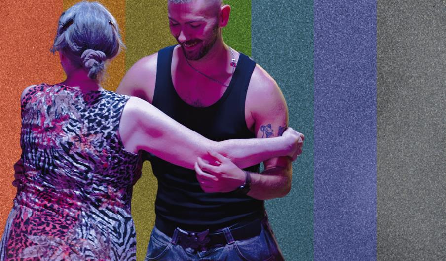 A man and a woman dancing in front of a glitter rainbow background
