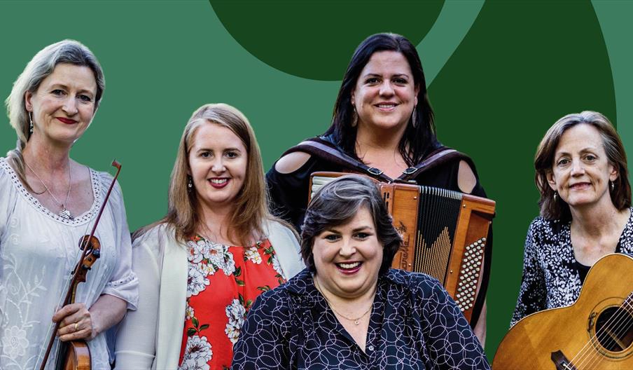 A group of 5 women holding traditional music instruments and smiling, with a green background.