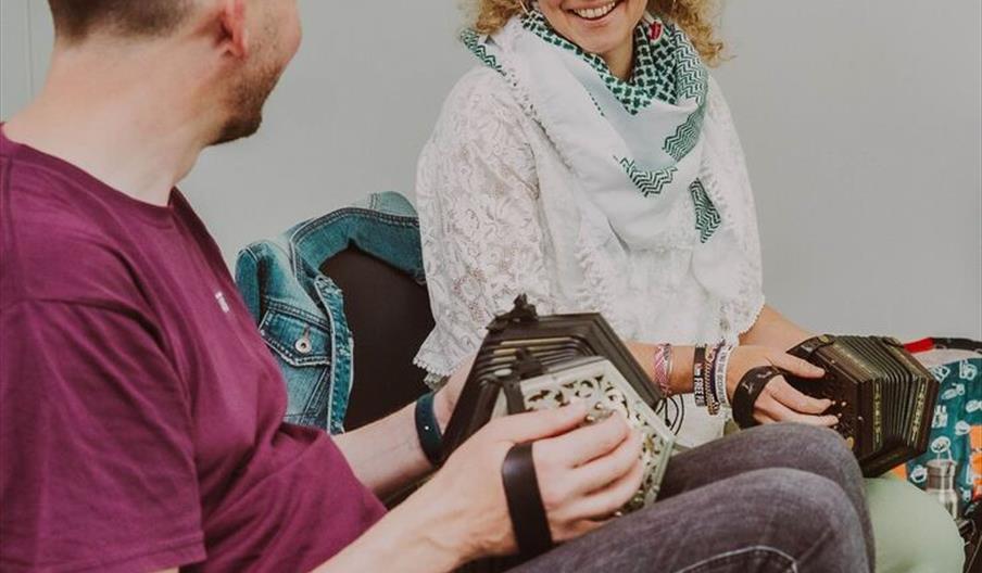 Lorraine Ní Bhriain and another person (who's face is not visible) both sit with their concertinas