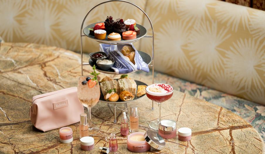 Afternoon Tea stand featuring sweet and savoury items, surrounded by ELEMIS Pro-Collagen Rose collection skincare items on the table