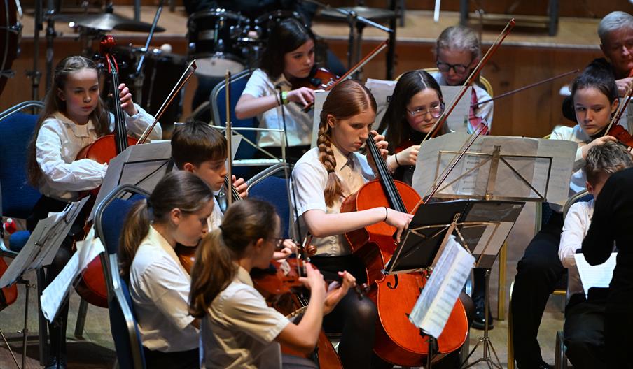 Students playing string instruments like violins and cellos in a concert.
