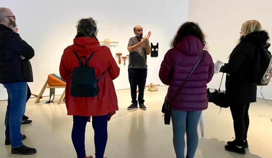 Picture of a BSL gallery tour. A gallery tour guide is presenting artworks to an audience