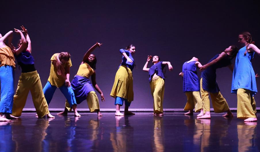 Picture of nine dancers in blue and yellow dancing on stage
