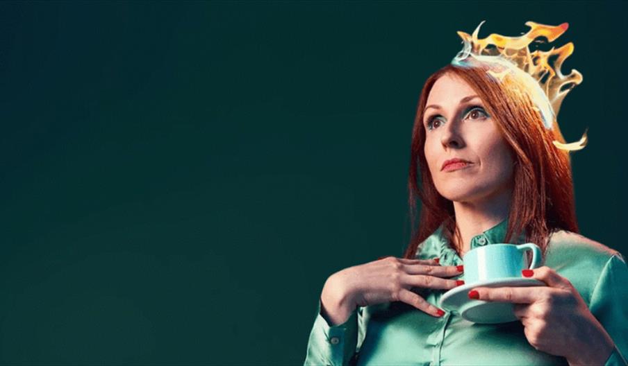 Photo of Suzy Crothers looking away with a cup of tea in her hand. She is dressed in blue, the tea cup and the background are also blue. Her hair is o