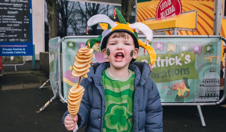 A child celebrates St Patrick's day in festive clothing and holds food on a stick