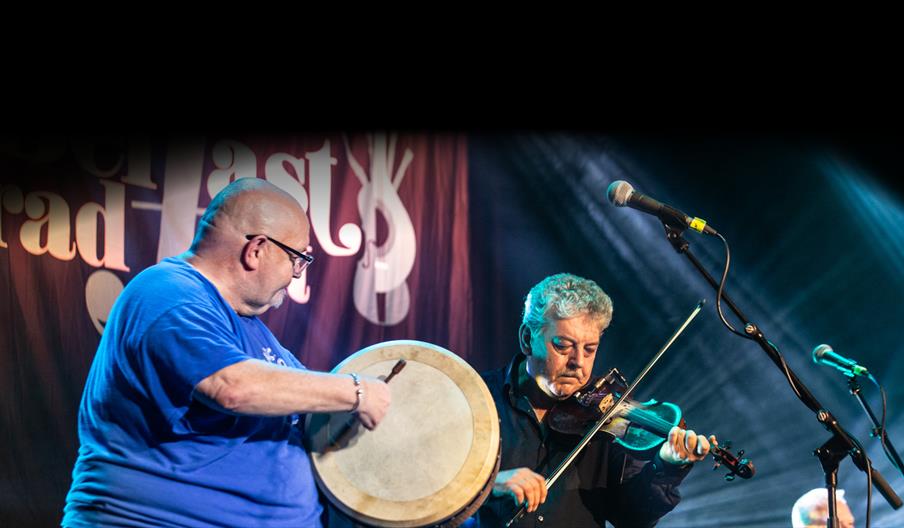 Two musicians playing the fiddle and the bodhrán on stage.