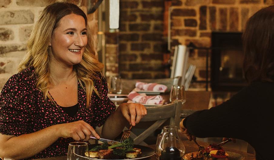 This image shows a female with blonde curly hair in floral purple dress enjoying a meal with a friend in Fratelli