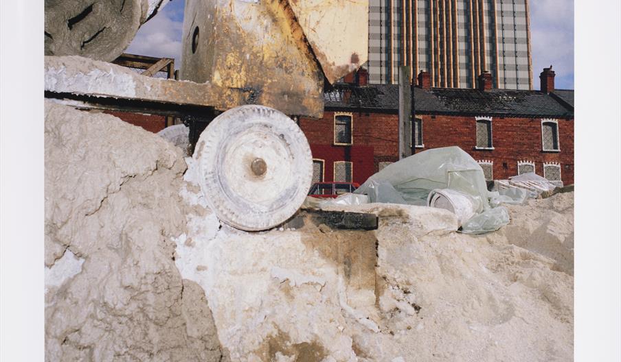 Photograph of a construction site with a large cement mixer in the foreground. Behind it are red-brick terraced houses and a tall modern building unde