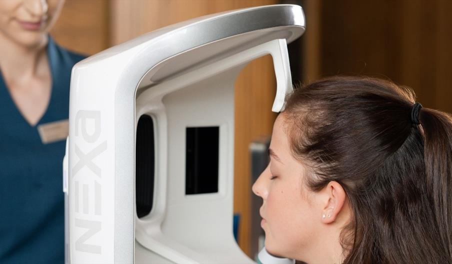 Brunette female having her face scanned by NEXA skin analysis machine with spa therapist