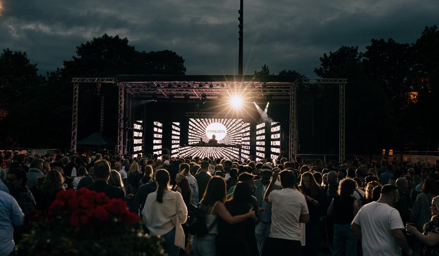 A crowd gathered outside to watch a stage with a DJ