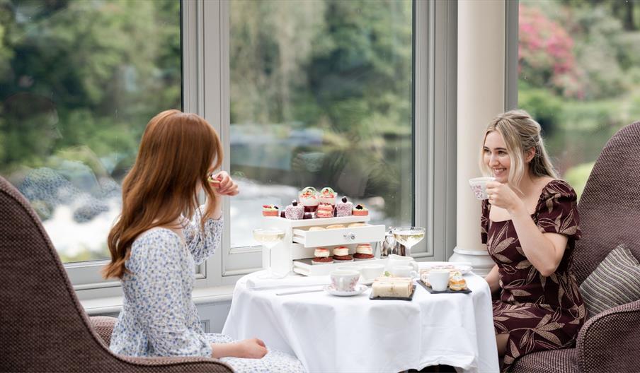 This image shows two females sitting in the Conservatory  enjoying afternoon tea by the window