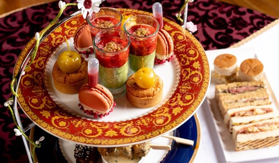 Tiered afternoon tea stand featuring colorful desserts, including layered parfait glasses, macarons, mini cakes topped with cherries, and delicate pas