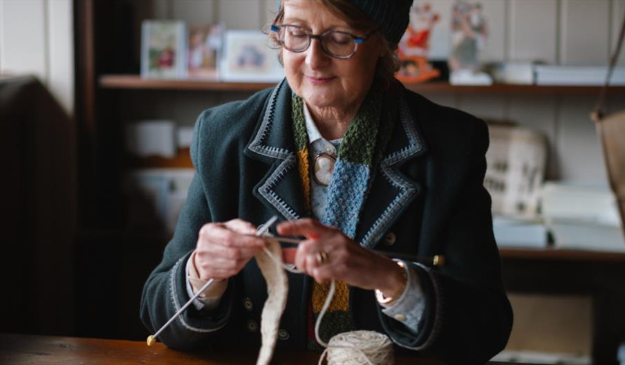 A lady in a blue coat dressed in period costume while knitting