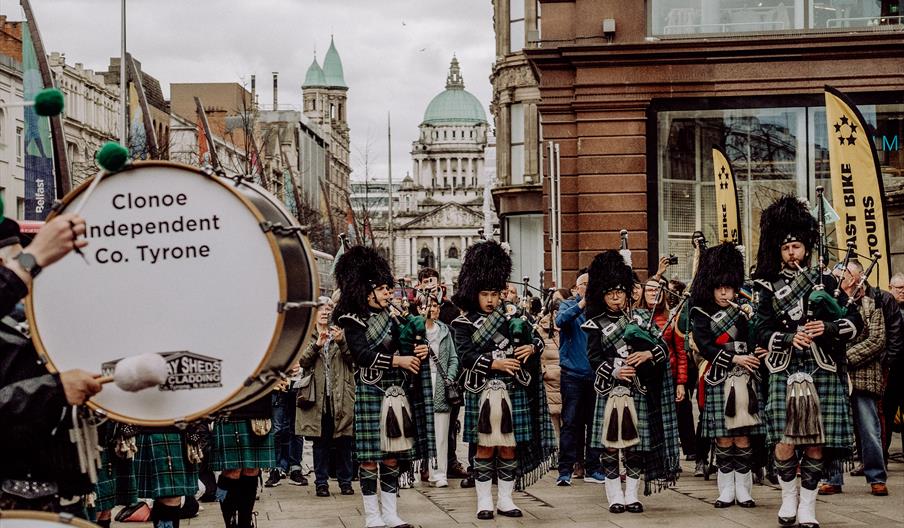 A pipe band plays in belfast city centre, the city hall is visible in the background