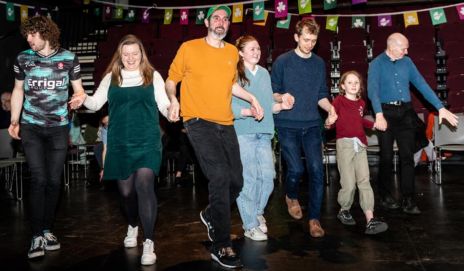 a group of 7 people of mixed ages dance together at the St. Patrick's Day Céilí