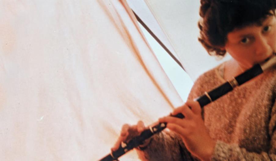A person with short dark curly hair plays a black and silver flute.