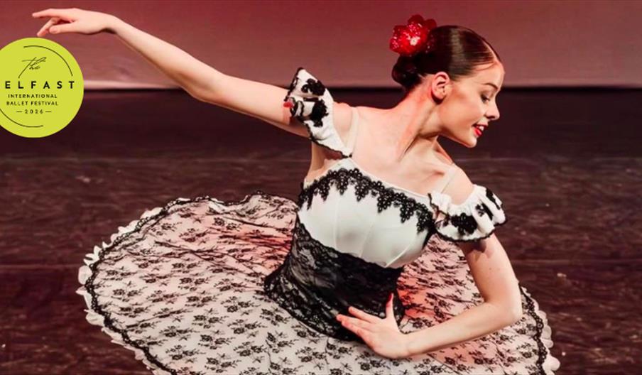 A ballerina bows on stage wearing a white and black lace ballerina dress with a red flower in her hair.