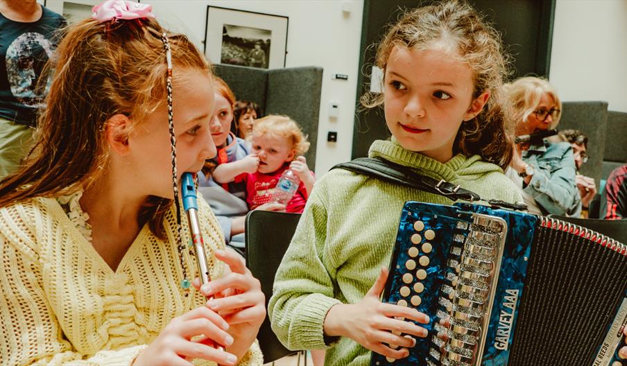 2 children, 1 plays tin whistle and the other plays accordion