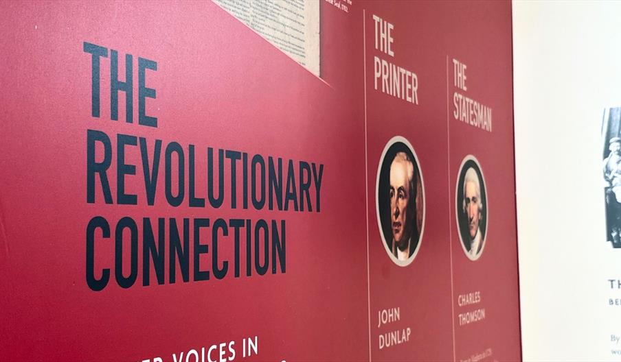 Close up shot of the exhibition stand. It has a solid red background with navy text that reads 'The Revolutionary Connection' on the left hand side, t