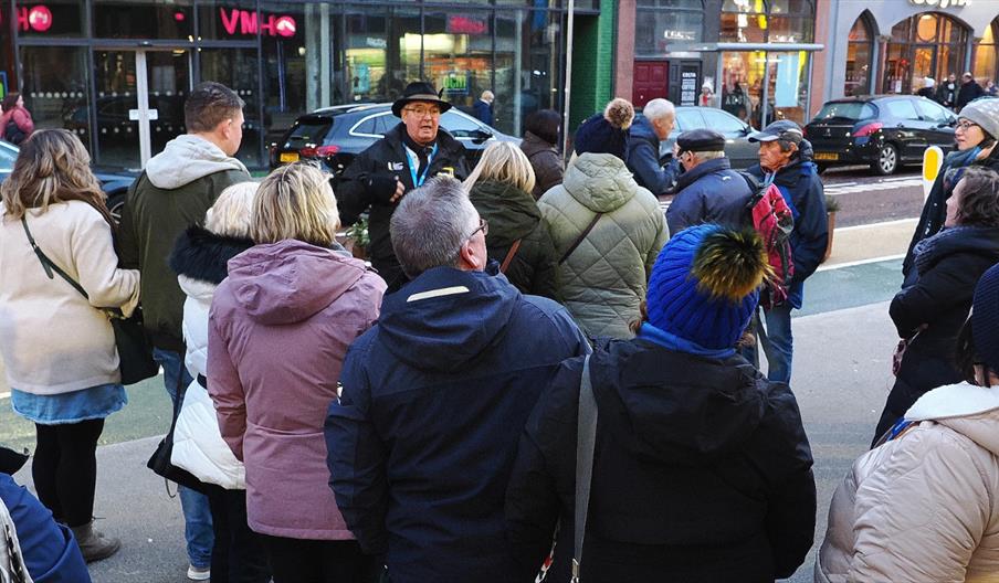 A group of people gathered on a street, listening to a tour guide speaking