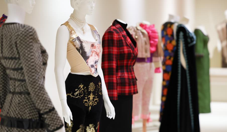 A series of white dummy models with fashion outfits on including a red plaid jacket and a cream corset