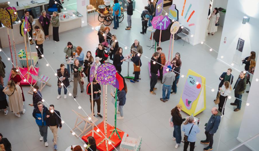 A variety of people standing in the atrium at ulster museum chatting and having drinks