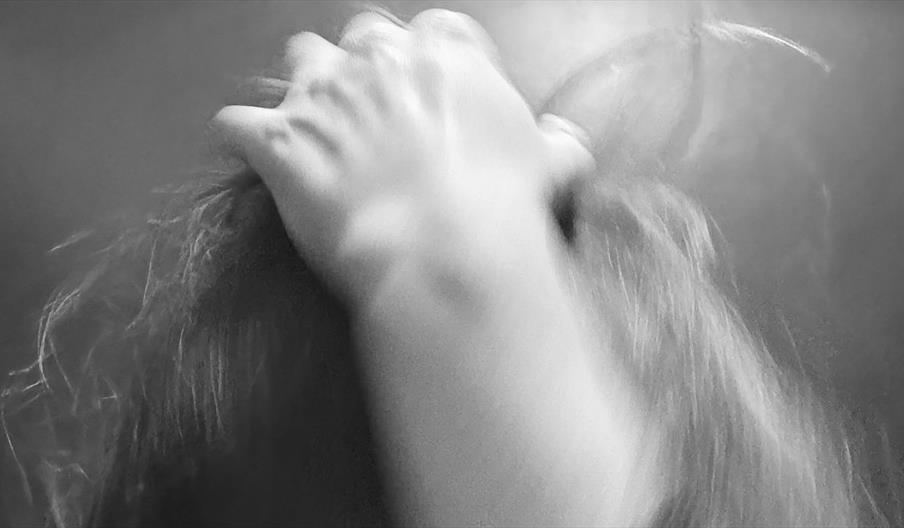 black and white blurred close up image of a person resting their hand on their head of mussed hair.