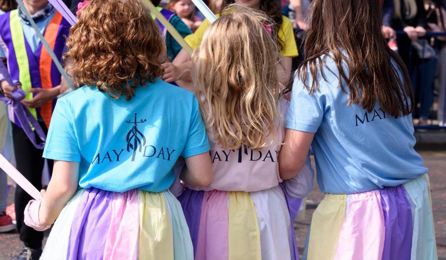 Children in pastel "May Day" shirts holding ribbons during a May Day dance