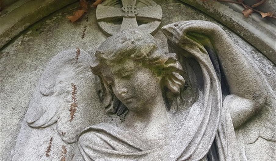 Stone angel sculpture with wings and a halo, head bowed in a solemn pose.