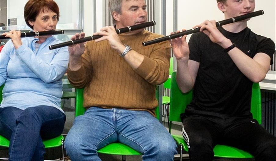 3 people sitting together playing the flute