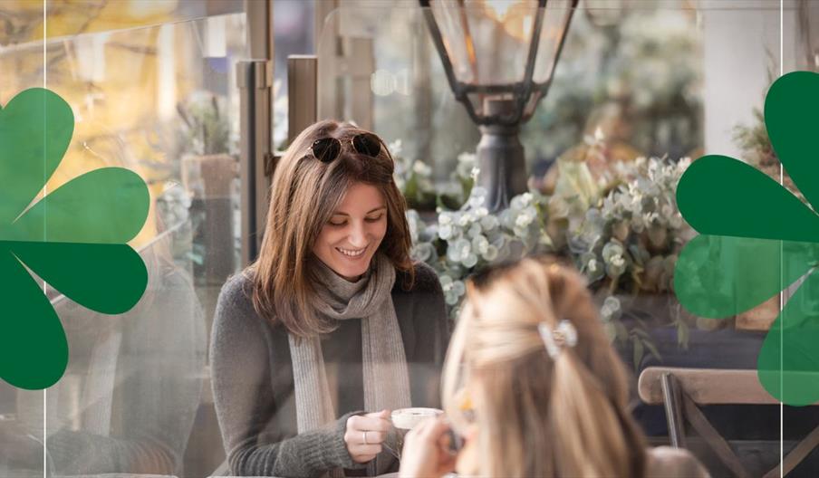 Brunette female holding an irish coffee with the back of a blonde hair female on the terrace at Parisien