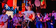 Dancer in orange feathered wristbands and YAA t-shirt dances in front of crowd on dance floor.