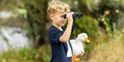 A child looking through binoculars whilst holding a duck teddy at WWT Castle Espie