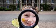 Child looking through magnifying glass with Mount Stewart House in the background
