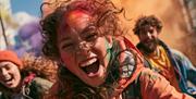 A young girl laughs at the camera while covered in colour powder.