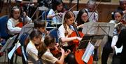 Students playing string instruments like violins and cellos in a concert.