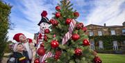 Two children enjoying festive Christmas decorations beside a tree adorned with red baubles, candy-cane ribbons and a nutcracker, with Hillsborough Cas