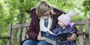 An adult and child sitting together on a garden bench reading The Gruffalo's Child.