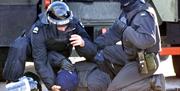 A wounded police officer on the ground is helped by two colleagues dressed in protective riot clothing.