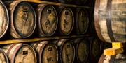 Rows of wooden whiskey barrels stacked on racks inside a dimly lit distillery warehouse.