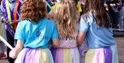 Children in pastel "May Day" shirts holding ribbons during a May Day dance