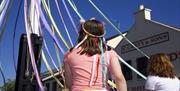 Child in a flower headband holding ribbons during a Maypole dance on a sunny day.